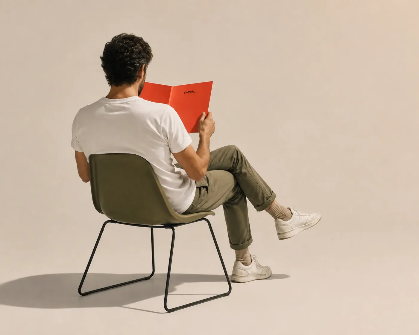 A person seen from behind in a chair, reading a coral thePath booklet.